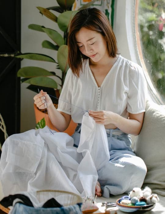Mujer cosiendo a mano una prenda blanca, sentada en un sillón